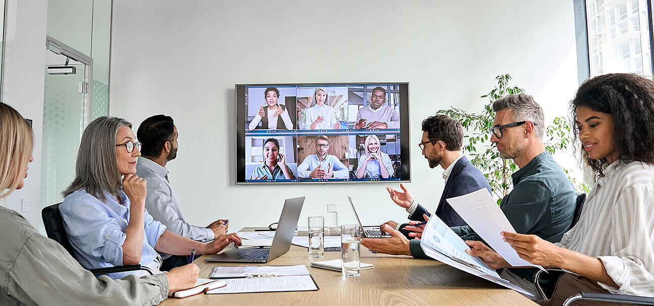 © insta photos - AdobeStock.com Business team in video conference with colleagues on large screen