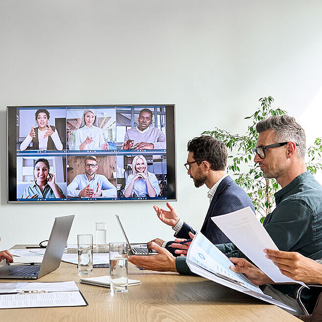 © insta photos - AdobeStock.com Business team in video conference with colleagues on large screen