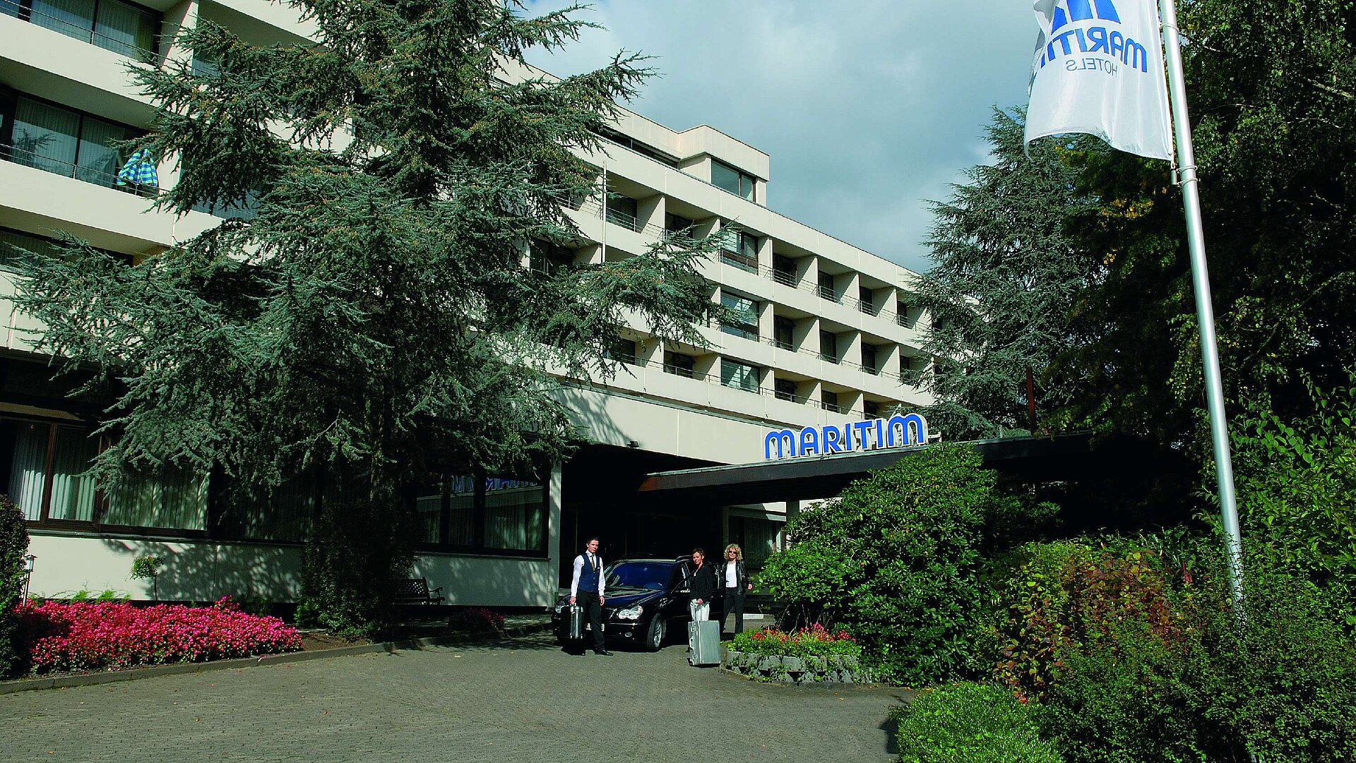 Entrance of the hotel Guests arrive at Maritim Hotel Bad Salzuflen surrounded by trees and landscaped greenery
