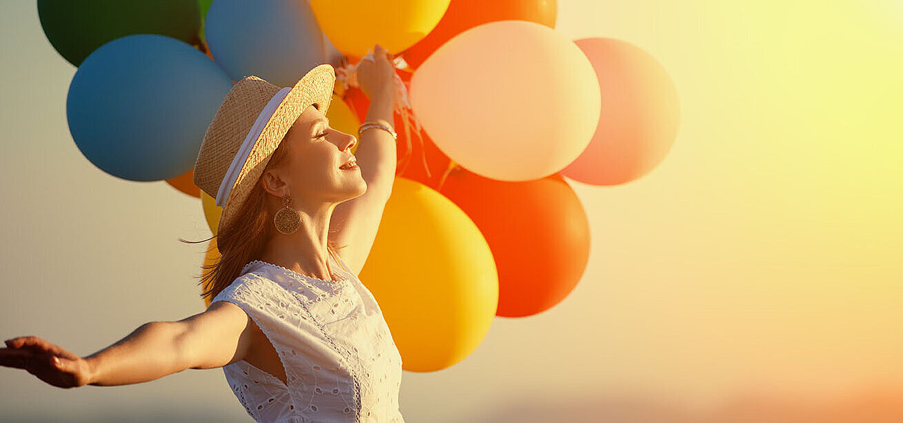 © JenkoAtaman - AdobeStock.com Woman with colourful balloons at sunset