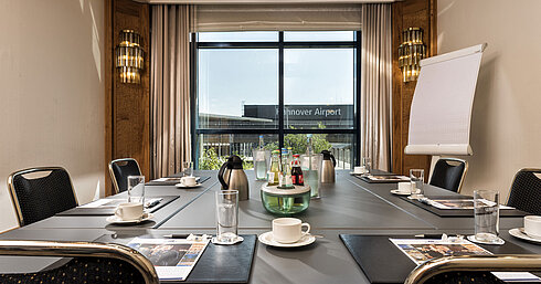 Salon Laves Bright meeting room with a conference table, drinks, and a view of the airport at Maritim Hotel Hannover.