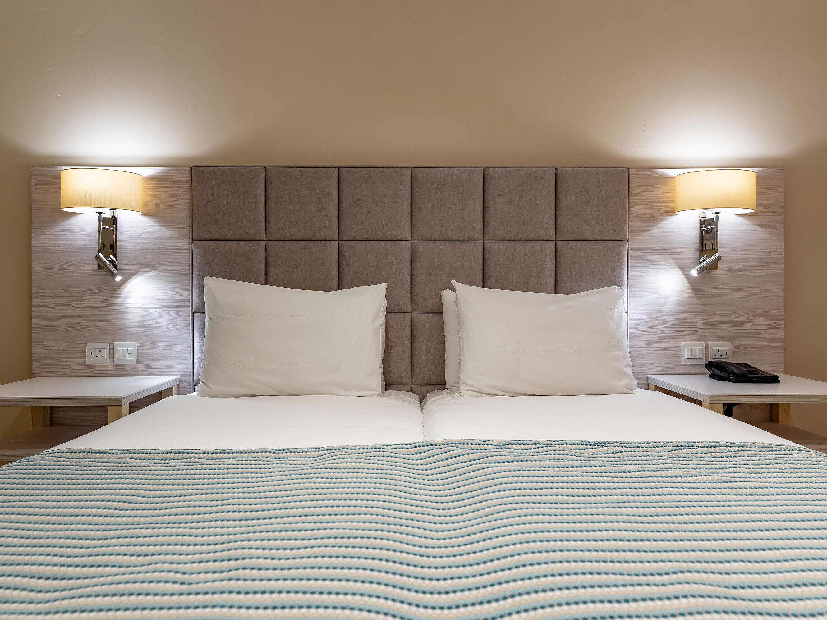 Economy room Classic double bed with padded headboard, bedside tables and reading lamps in a hotel room