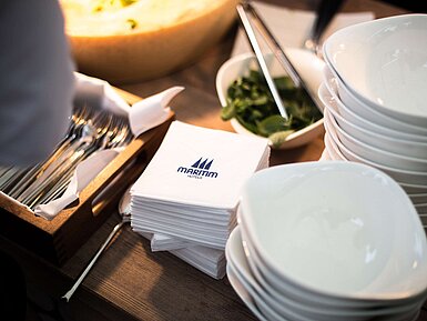 Geschirr auf einem Buffet Stacked white bowls, Maritim-branded napkins and cutlery arranged on a buffet station.