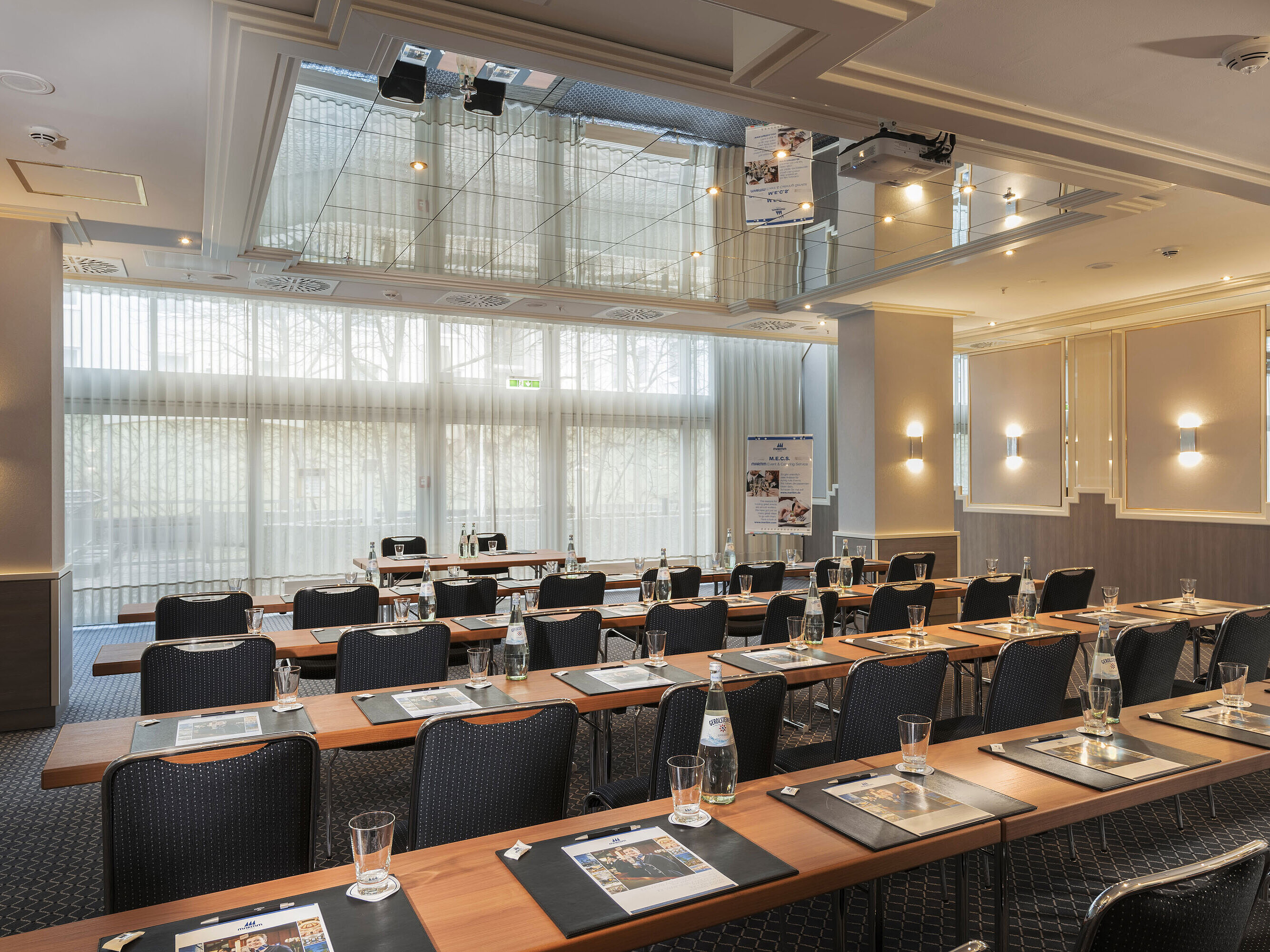Saal München Meeting room with large windows, tables and water bottles at the Maritim Hotel Munich