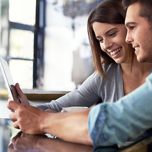 © peopleimages.com - AdobeStock.com Young couple sitting in café looking together at a tablet