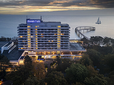 Exterior view Evening view of Maritim Seehotel Timmendorfer Strand with illuminated pier and a sailboat in the background at sunset.