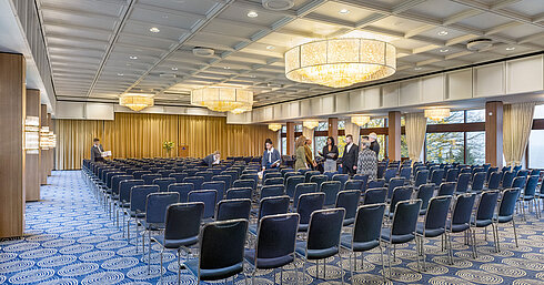 Saal Maritim Saal Maritim in the Maritim Hotel Kiel, large conference room with row seating, chandeliers and stage, staff prepare the room.