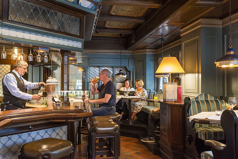 Friesenstube Restaurant Cozy hotel bar in traditional style with guests enjoying drinks and a bartender pouring beer.