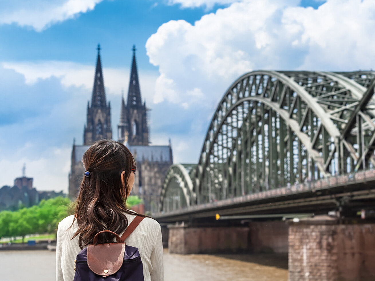 © 75tiks - AdobeStock.com Woman with backpack looking at Cologne Cathedral and Hohenzollern Bridge by the Rhine