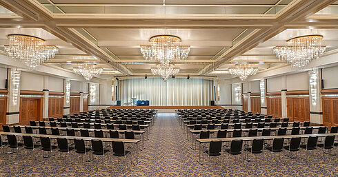 Fürst-von-Metternich-Saal Fürst-von-Metternich Hall with large stage, row seating, elegant chandeliers and bright interior.