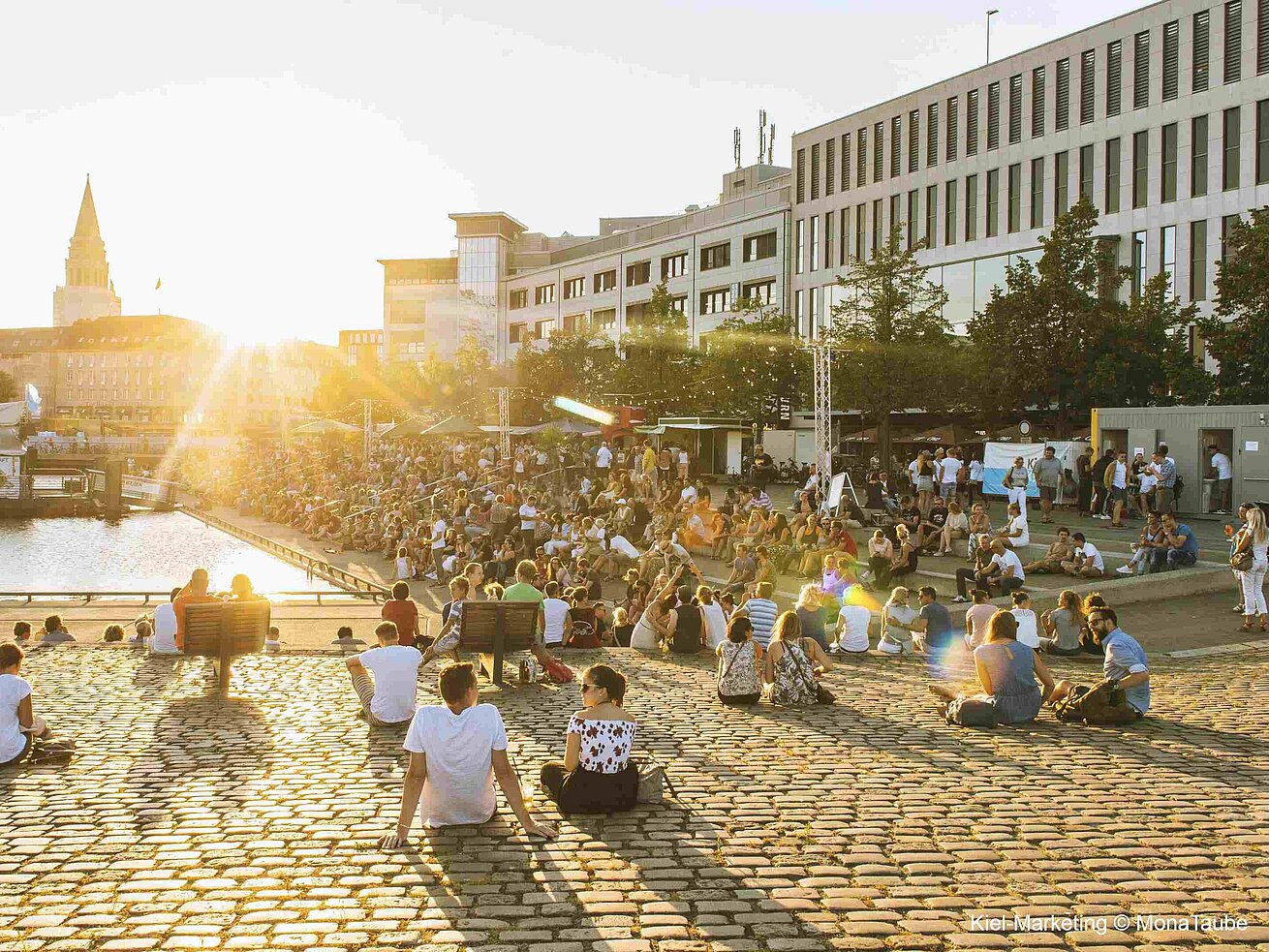 Kiel Marketing © Mona Taube People relaxing by riverside with city buildings in background at sunset