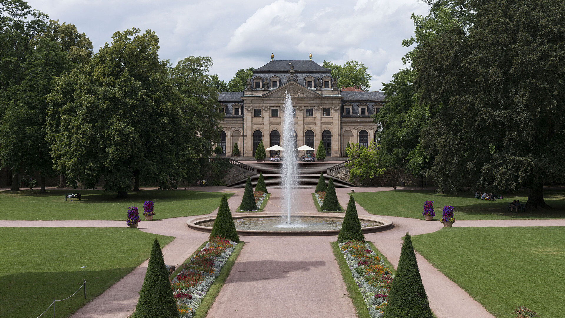 Exterior view The baroque Orangerie Fulda with palace garden, fountain, and manicured flower beds in the foreground.