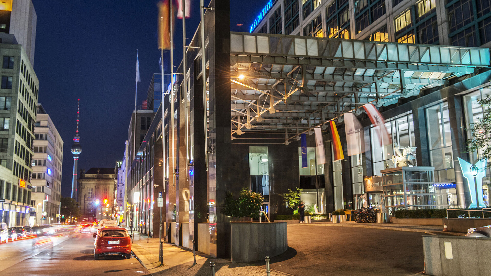 Entrance of the hotel Night view of the illuminated entrance of Maritim proArte Hotel Berlin with TV tower in background and flags.