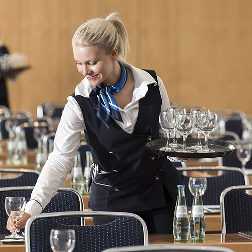 Maritim Conference Service A service staff member at the Maritim Berlin sets up a conference room, carrying a tray of glasses and placing water bottles.