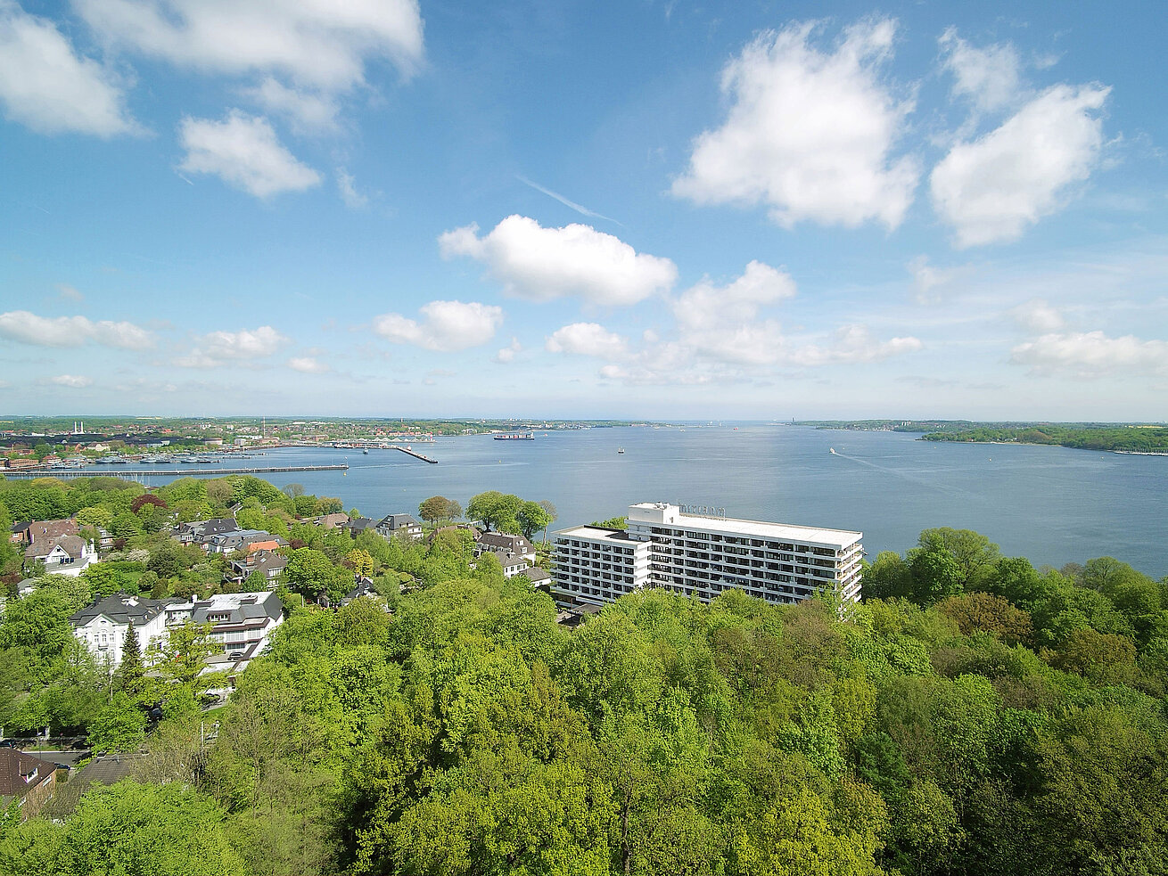 Exterior view Aerial view of the Maritim Hotel Kiel, surrounded by green countryside and the Kiel Fjord, under a bright blue sky.