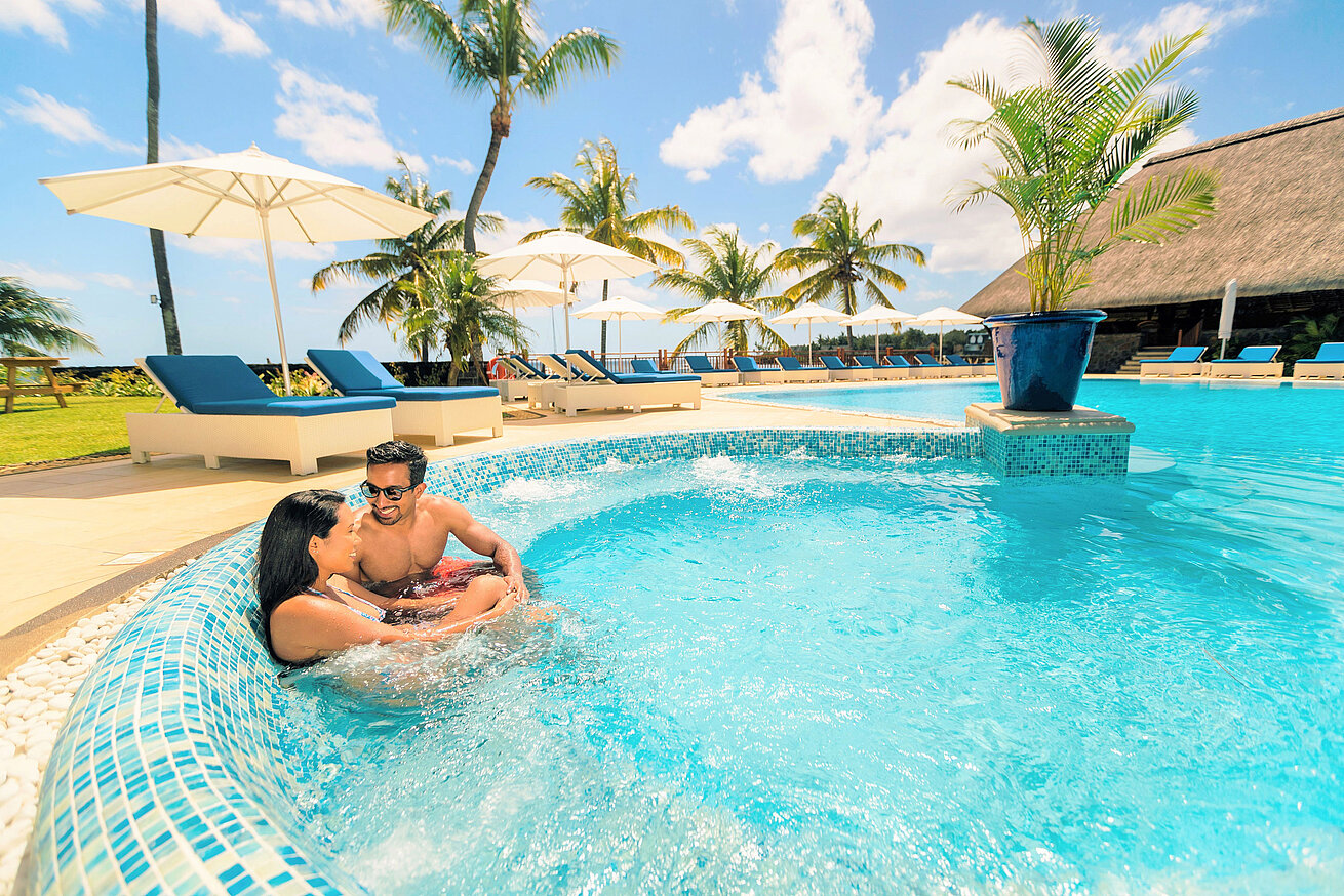 Pool Couple relaxing in hotel pool with palm trees, sun umbrellas and blue sky