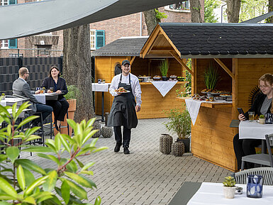 Outdoor terrace Waiter serving food at an event on the terrace of the Maritim Hotel Darmstadt with wooden huts