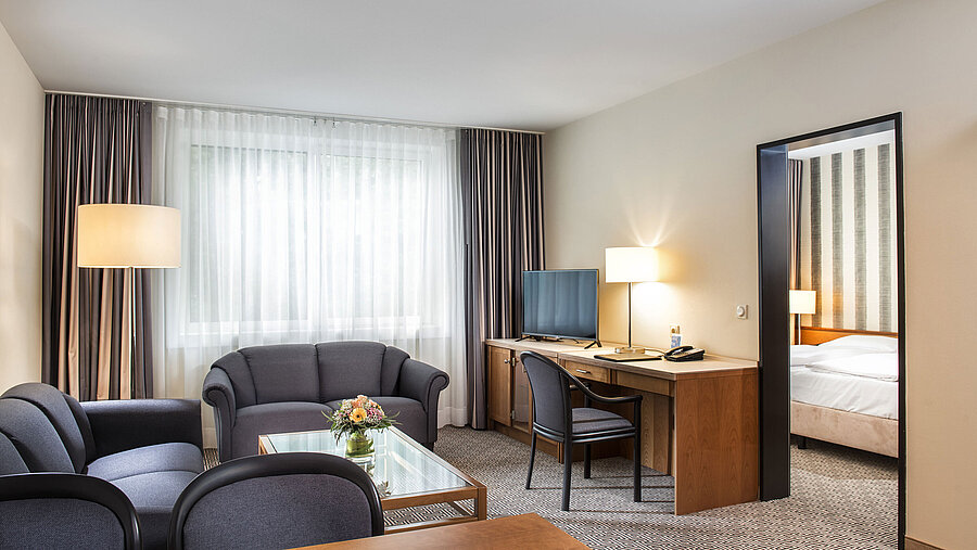 Junior suite Living area with sofas, TV, desk and access to bedroom at Maritim Hotel Stuttgart