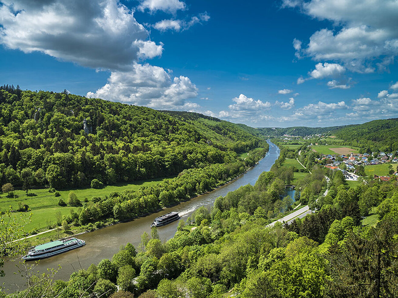 © Andy Ilmberger - AdobeStock.com Boats on the Altmühl River in the Altmühltal, surrounded by green hills and blue sky