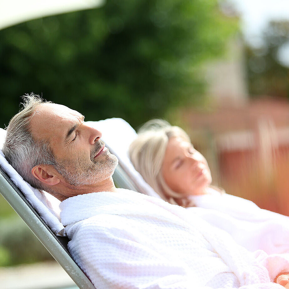 © goodluz - AdobeStock.com Man and woman in bathrobes relaxing on outdoor loungers and enjoying a peaceful break.