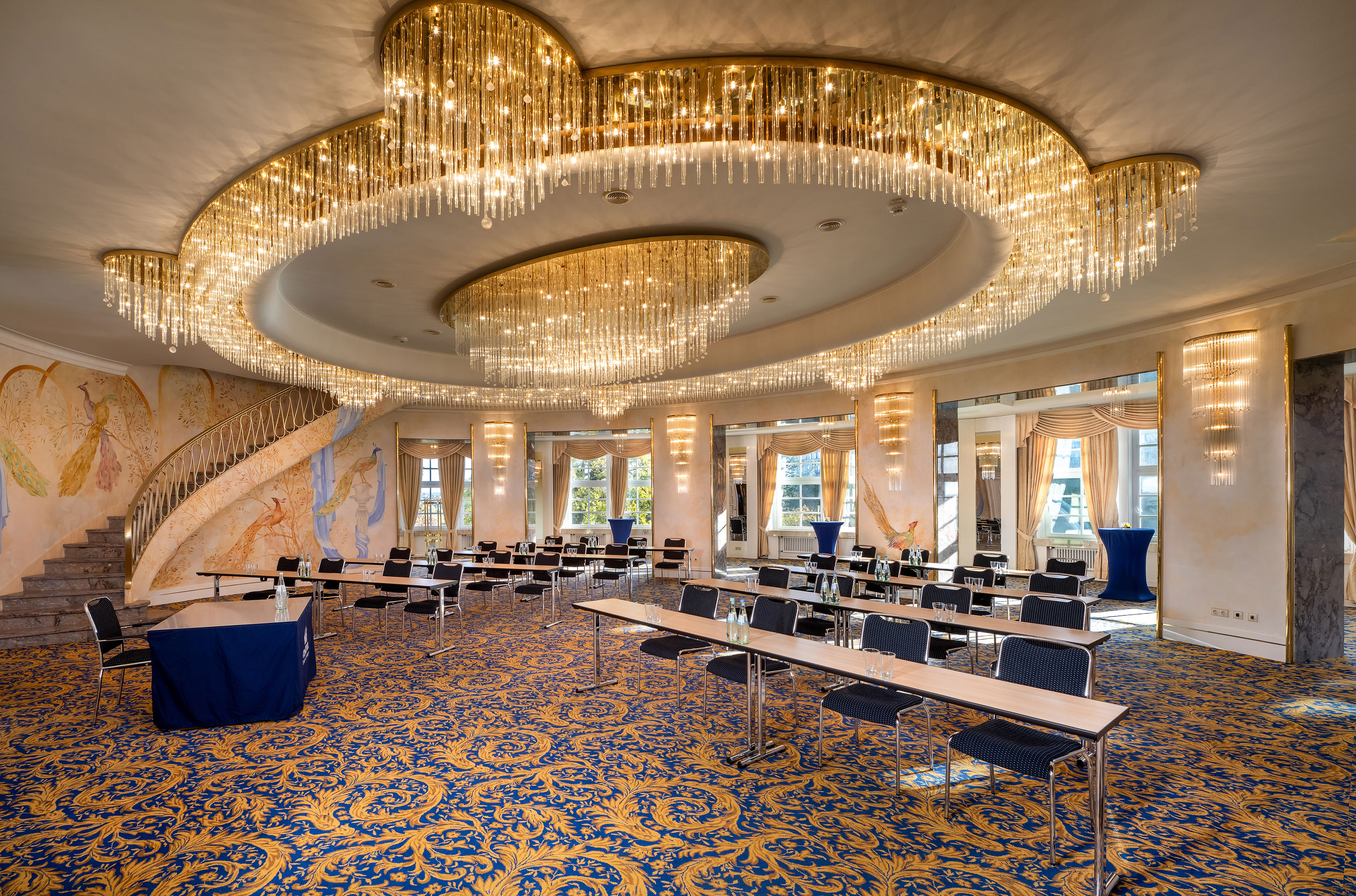 Fürst-von-Pückler-Saal Fürst-von-Pückler Hall with large windows, row seating, striking ceiling lights and a bright interior.