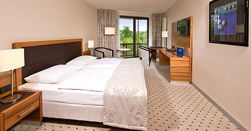 Comfort room Bright room at Maritim Hotel Bad Homburg with cozy bed, desk, and balcony with green view.