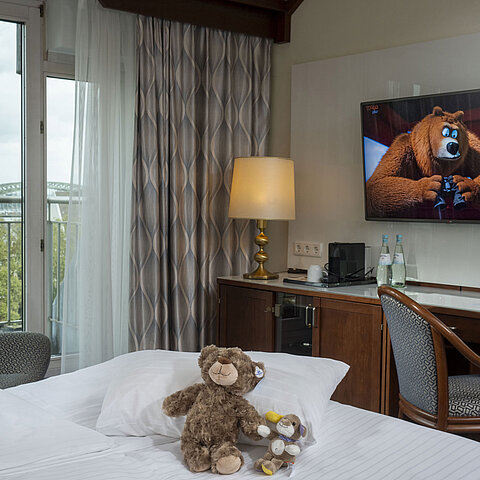 Camera familiare presso l'Hotel Maritim Colonia con TV, peluche sul letto e vista sul Reno.