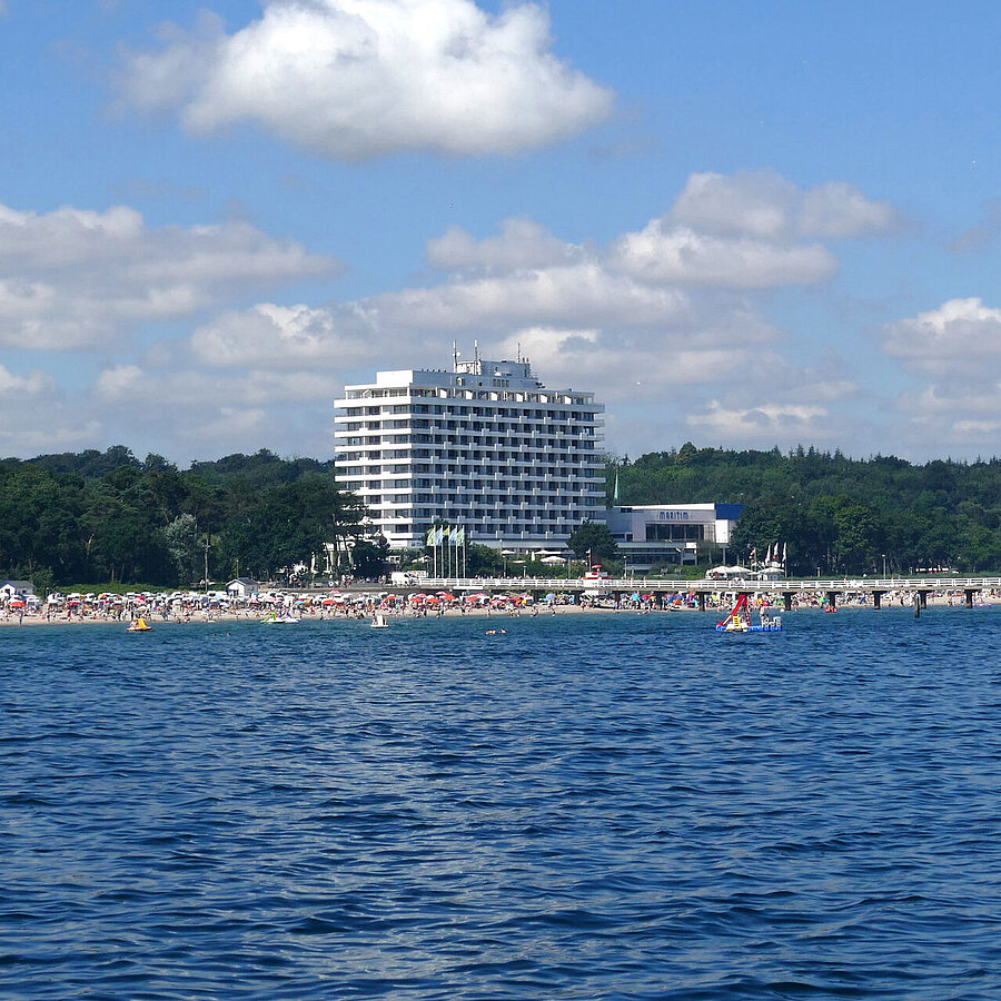 Exterior view Maritim Seehotel Timmendorfer Strand, pier, and colorful flags from a boat on a sunny day.