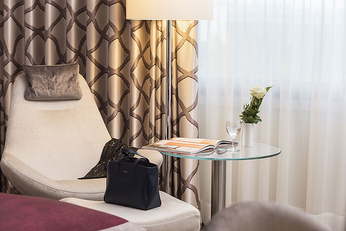 Detail of the hotel room Detail of a Classic room at Maritim Hotel Bonn with a cozy chair, curtain, table, glass, rose, and a handbag.