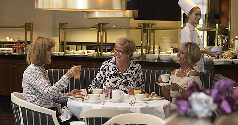 Park restaurant with sun terrace Three women enjoying a relaxed breakfast at Maritim Hotel Bad Homburg, served by a friendly chef.
