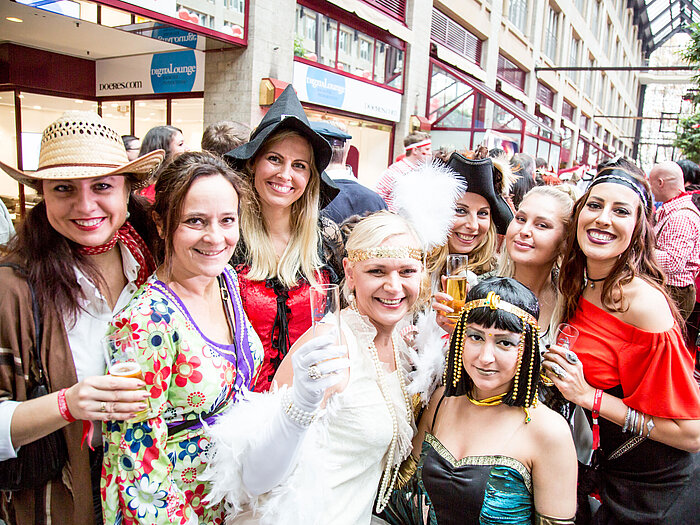 Women in colorful costumes celebrate at a carnival and hold champagne glasses up to the camera.