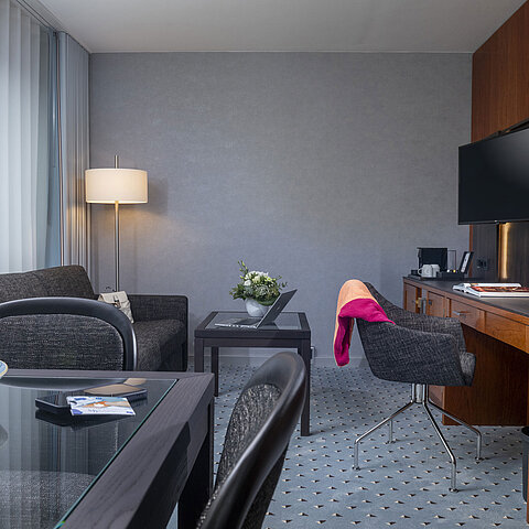 Elegant suite living room at Maritim Hotel Bremen with cozy seating area, desk, TV, and fresh flowers for decoration.