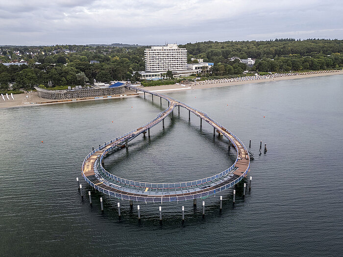 Pier in front of the Maritim Seehotel Timmendorfer Strand with calm water and blue sky.