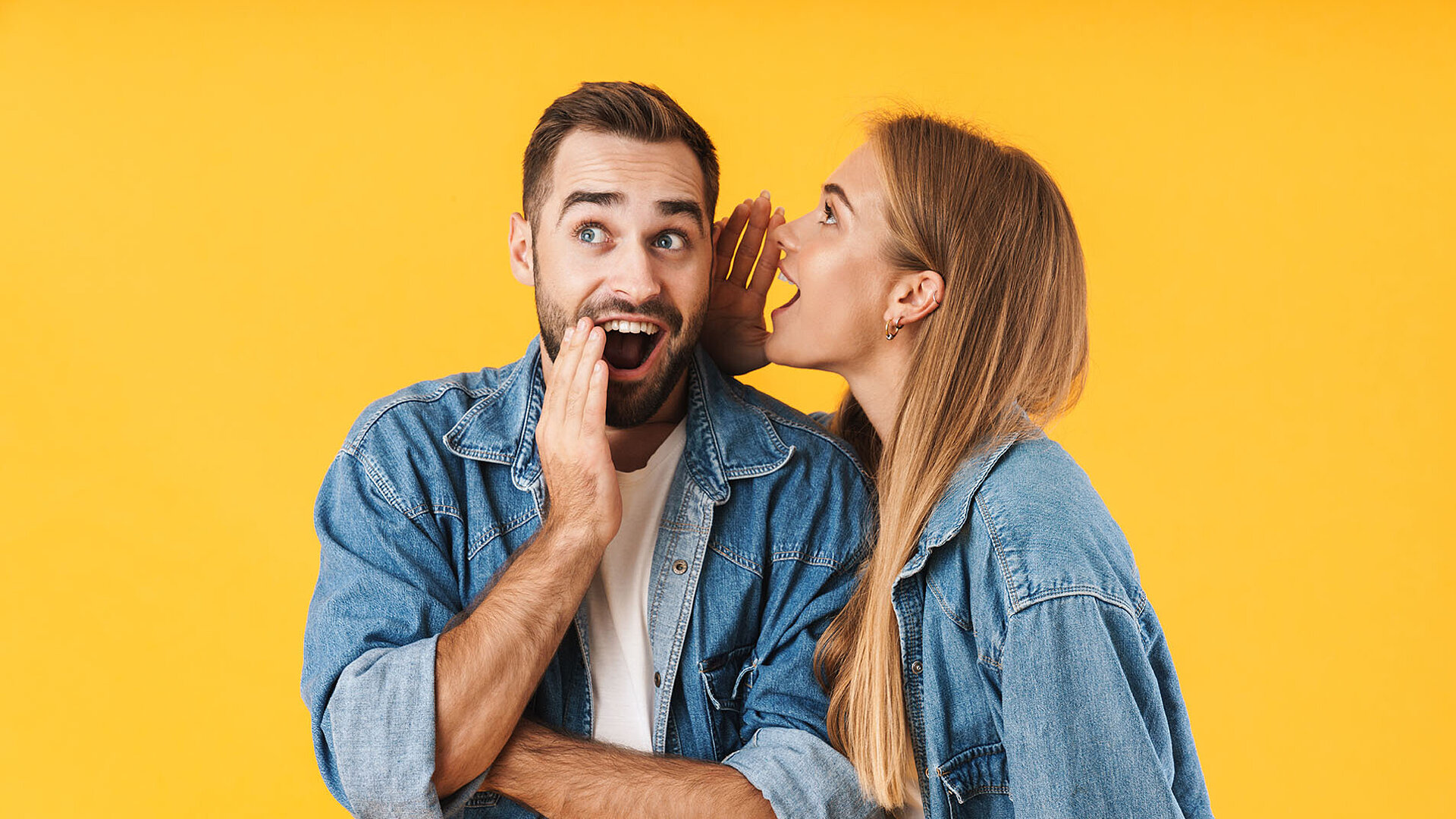 © Drobot Dean - AdobeStock.com Woman whispers secret to man, both laughing in denim jackets against yellow background