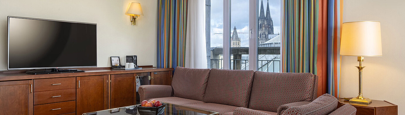 Suite Senior Soggiorno della Senior Suite al Maritim Hotel Köln con divano, TV e vista sul Duomo di Colonia.