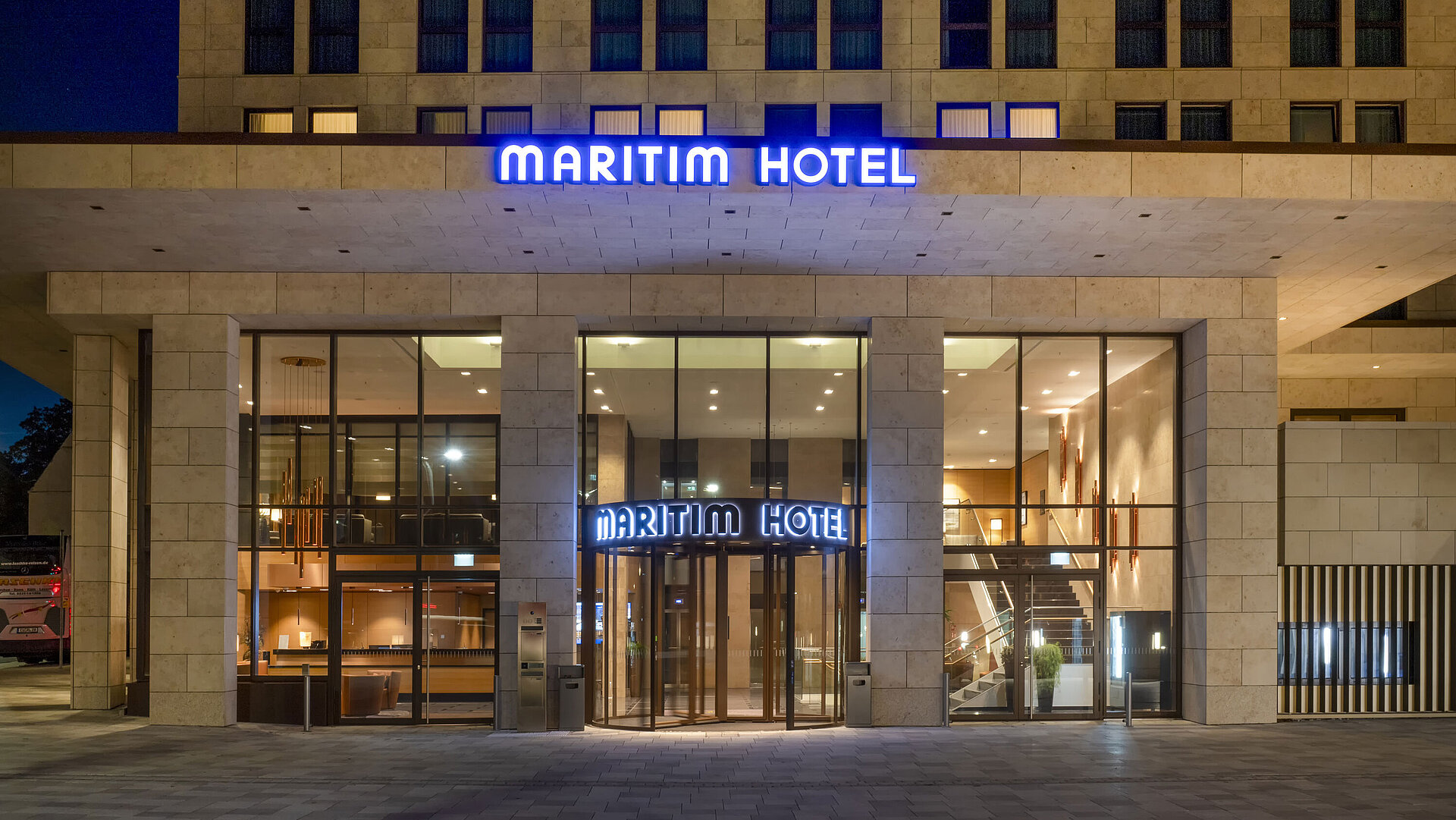 Exterior view Illuminated entrance of Maritim Hotel Ingolstadt with modern glass facade at night.