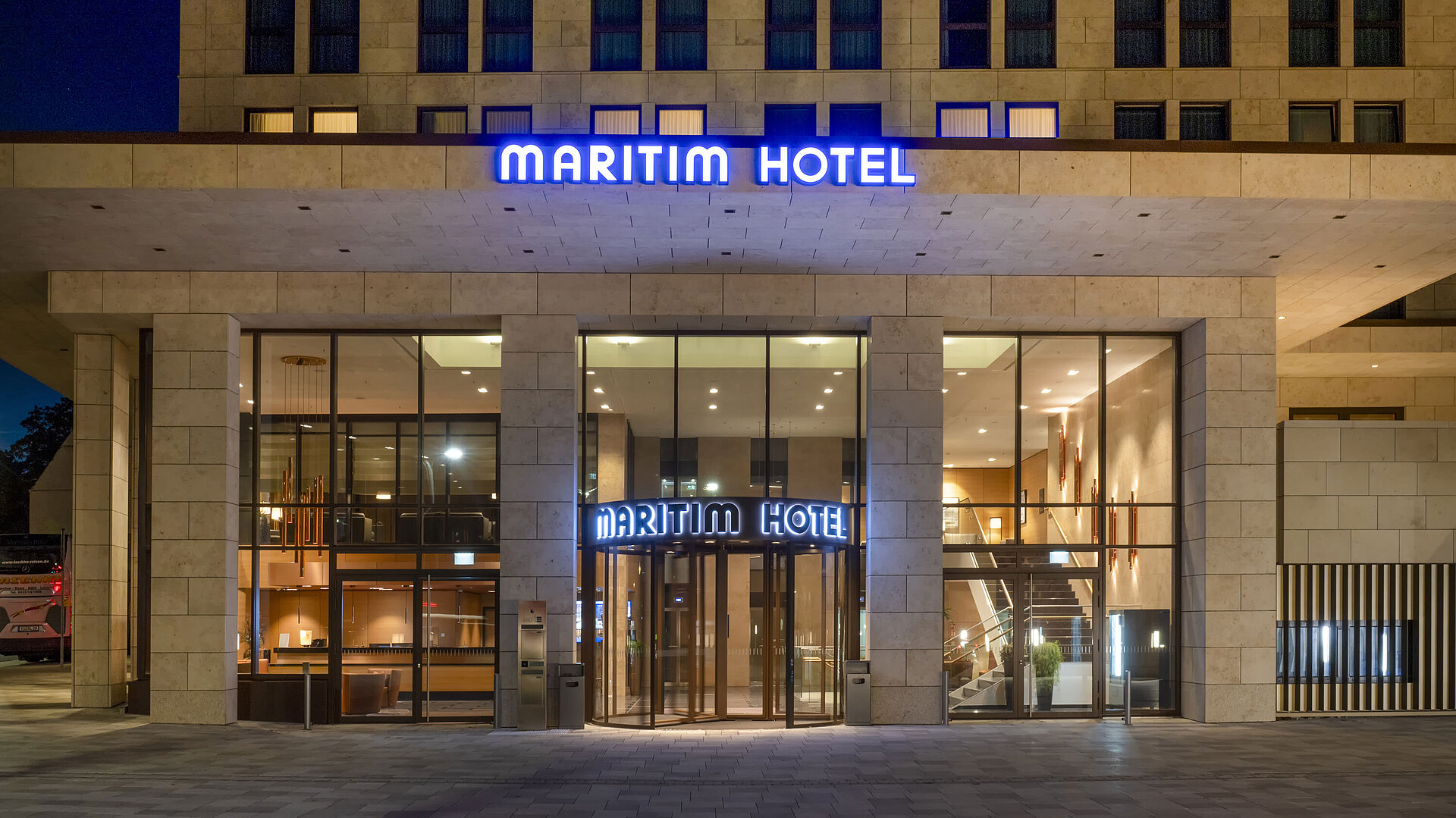 Exterior view Illuminated entrance of Maritim Hotel Ingolstadt with modern glass facade at night.